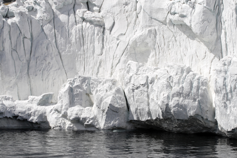 Zdjęcie przedstawia białą ścianę lodowca podcinaną przez morze