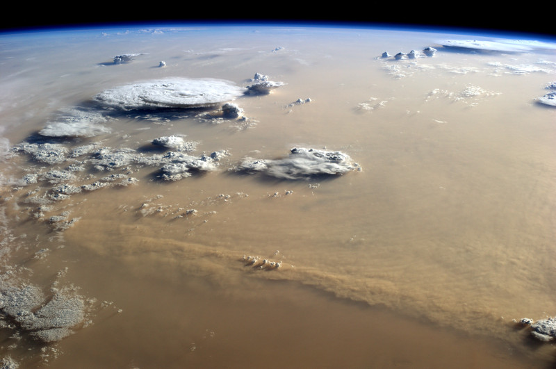 Burza piaskowa nad Saharą, zdjęcie z góry. Atmosfera jest żółta od pyłu, nie widać powierzchni Ziemi. Nad warstwę pyłu wystają wierzchołki rozbudowanych chmur burzowych. 