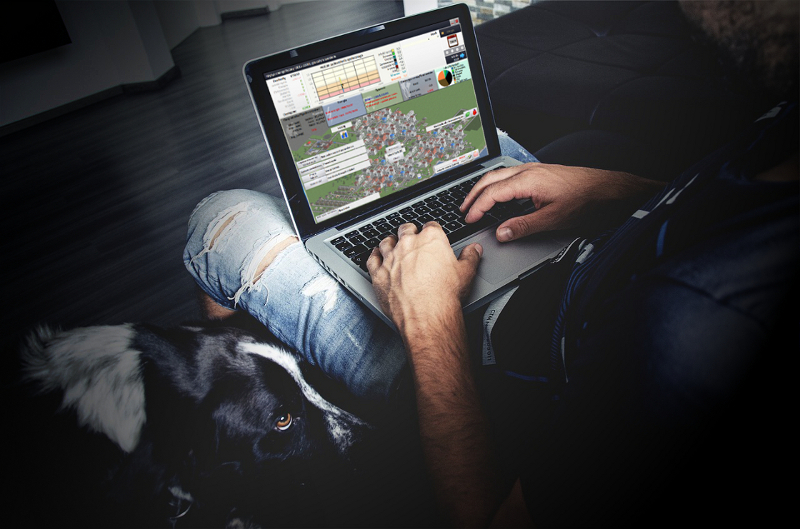 Zdjęcie przedstawia mężczyznę siedzącego z laptopem na kolanach, na ekranie widać grę Świat na rozdrożu