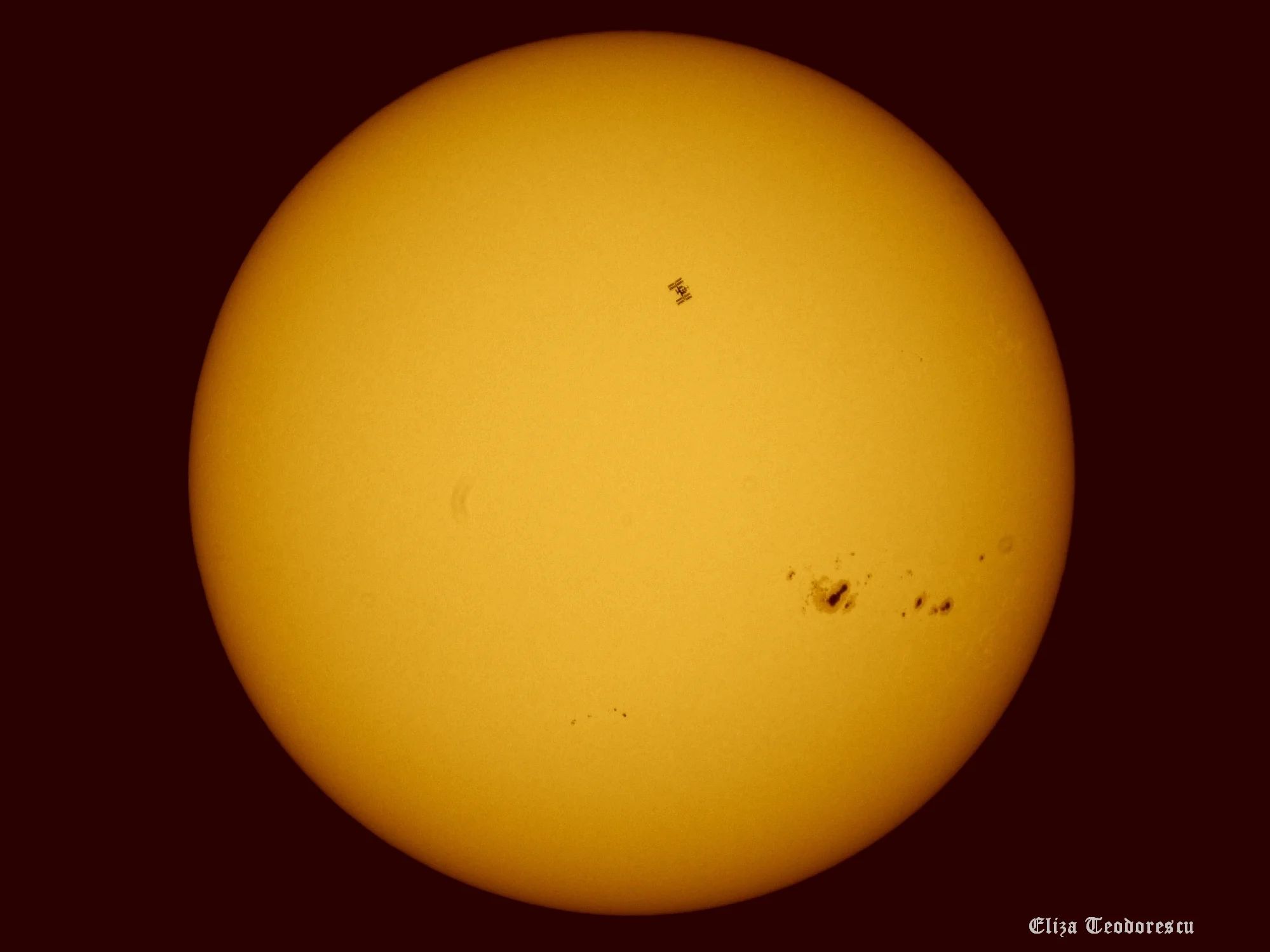 Zdjęcie Słońca. Widoczne są liczne plamy słoneczne oraz Międzynarodowa Stacja Kosmiczna na tle tarczy słonecznej