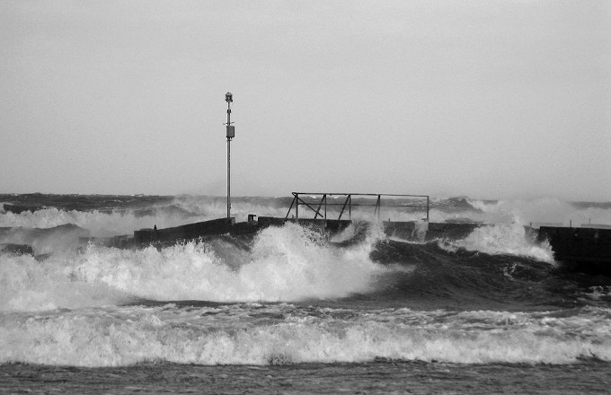 Zdjęcie: sztorm na Bałtyku. Grzywiaste fale atakują wysunięty w morze pomost ze małą stacją meteorologiczną na maszcie.