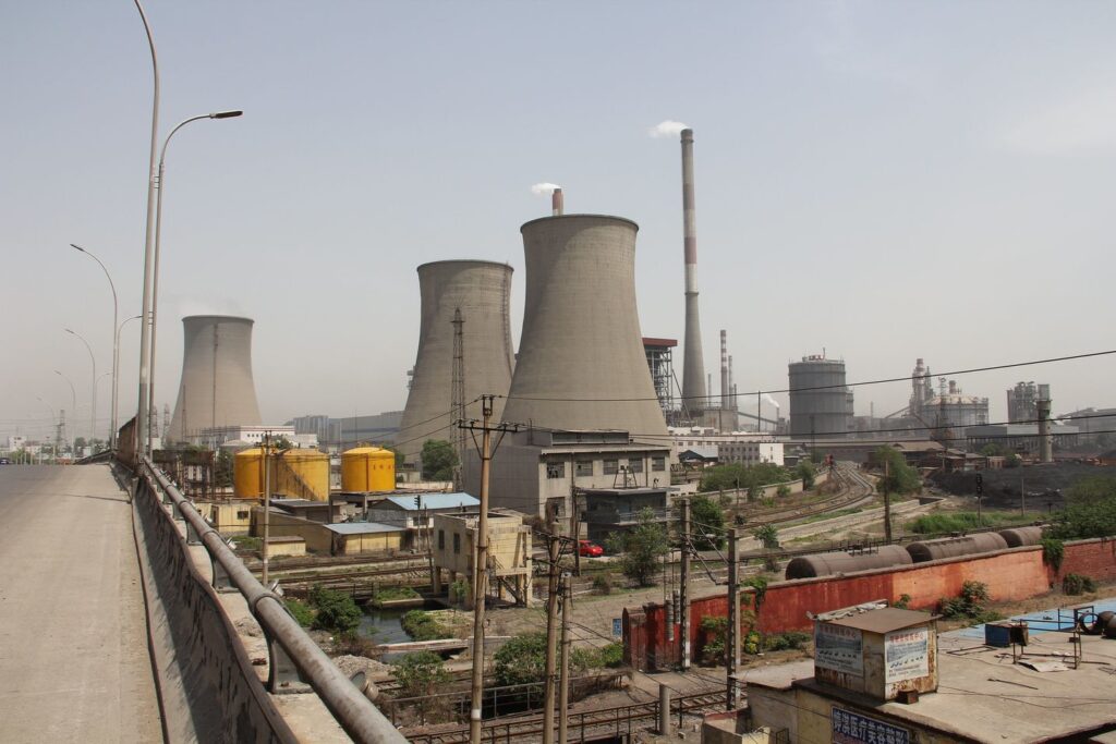 Zdjęcie: elektrownia węglowa w Hanan w Chinach, widoczne potężne chłodnie kominowe, kominy oraz tory kolejowe.