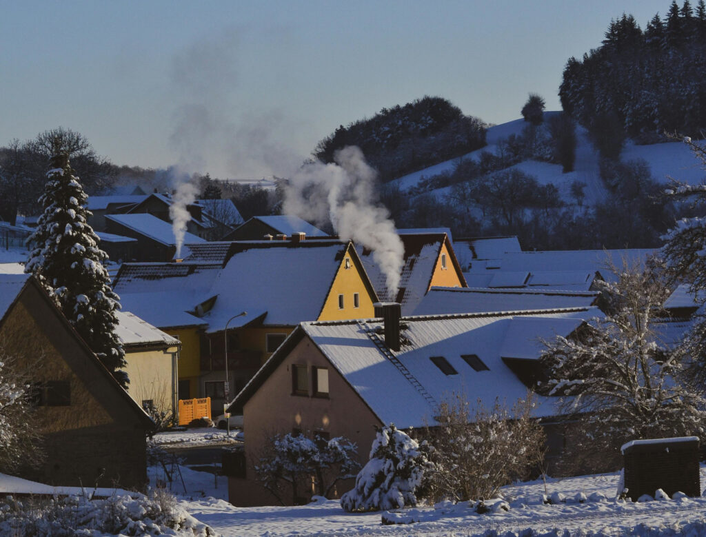 Zdjęcie ilustracyjne: wioska z kilkoma domami z kominami, z których unosi się dym.