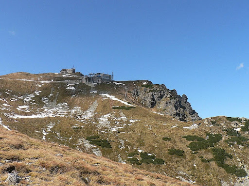 Zdjęcie: Kasprowy Wierzch od strony Doliny Gąsienicowej, widać skały pokryte suchą trawą, połacie kosodrzewiny, nad nimi skały i budynek Obserwatorium.