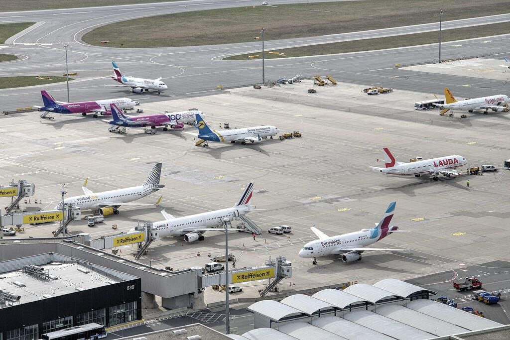 Zdjęcie: płyta lotniska z zaparkowanymi wieloma samolotami pasażerskimi. 