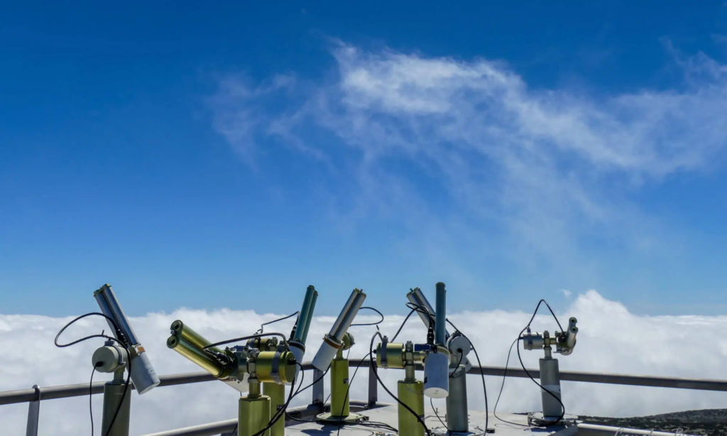 Zdjęcie: fotometry CIMEL ustawione na platformie pomiarowej w górach. W tle chmury.  