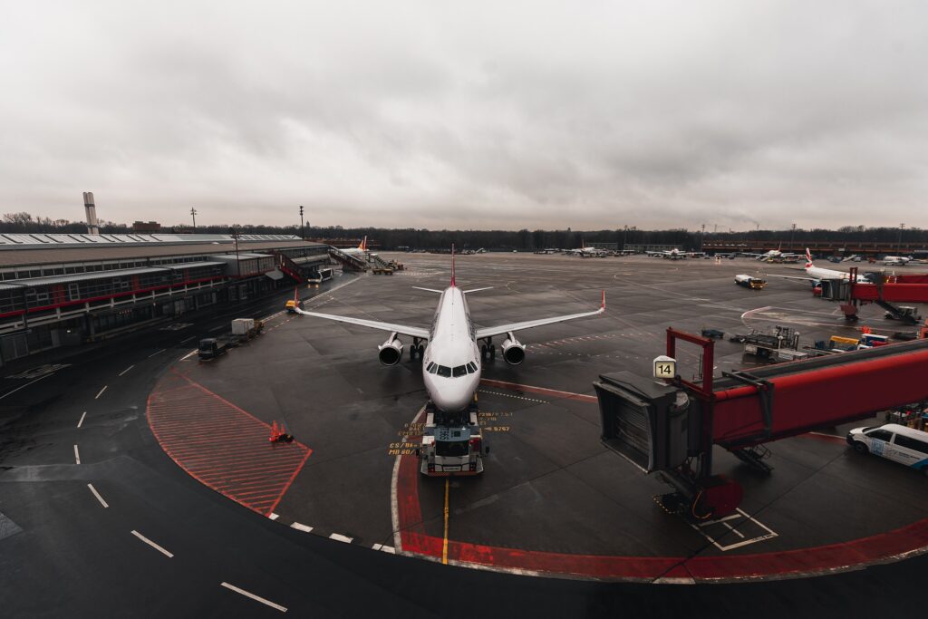 Zdjęcie: samolot na płycie lotniska, podprowadzany do rękawa przez specjalny pojazd.