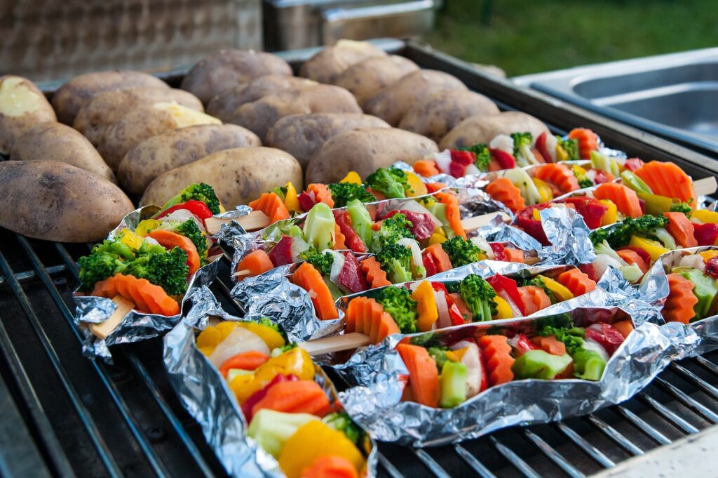 Zdjęcie: ziemniaki i szaszłyki warzywne ułożone na grillu. 