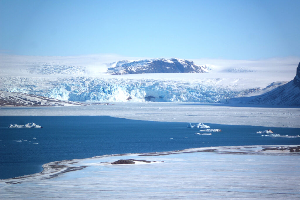 Zdjęcie: okolice Ny-Alesund, Spitsbergen. Zatoka częściowo pokryta lodem, na lądzie widoczny spływający do morza lodowiec.