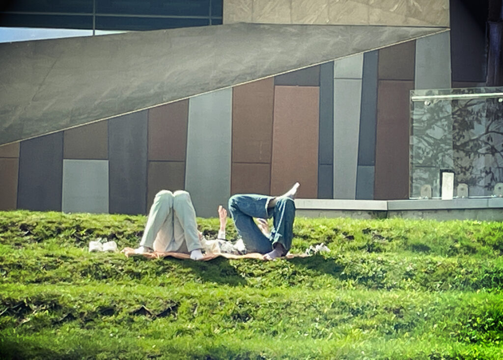 Zdjęcie: trawnik przy Centrum Nauki Kopernik w Warszawie. Widać nogi dwóch wylegujących się na słońcu osób. Wiosna, kwiecień 2023. 