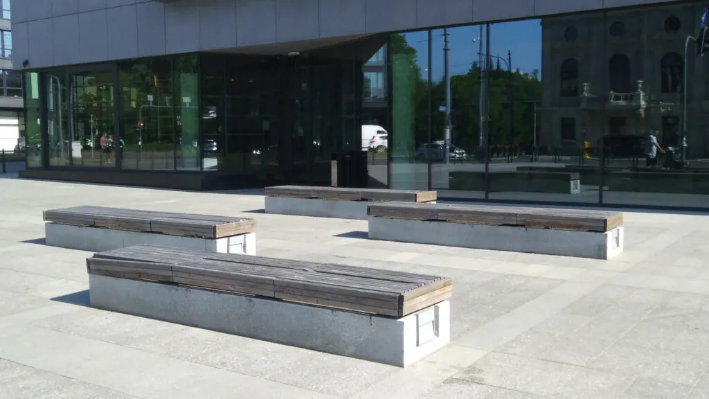 Zdjęcie dekoracyjne: ławki na betonowym dziedzińcu obok biurowca.