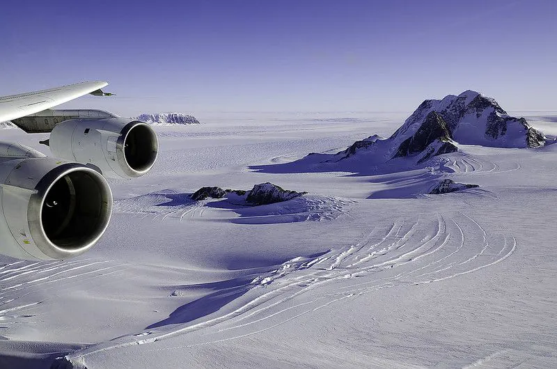 Zdjęcie: Antarktyda Zachodnia, Ziemia Marie Byrd. Widać skrzydło samolotu, z którego zrobiono zdjęcie i  pokryty śniegiem, pofałdowany krajobraz z pojedynczymi górami.