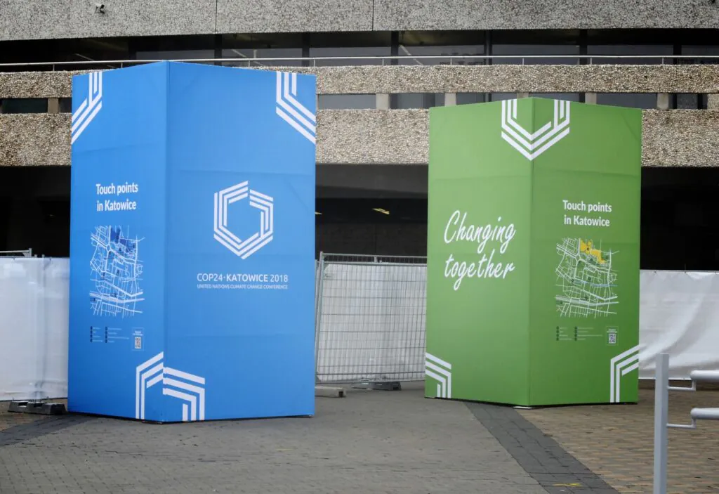 Zdjęcie: COP24, okolice Spodka, widać dwa dekoracyjne bloki, niebieski i zielony, z napisami „COP24 Katowice” i „changing Together”.