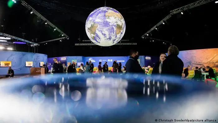Podsumowanie COP26. Zdjęcie: grupa osób dyskutujących w dużej sali konferencyjnej. Pod sufitem wisi duża, realistycznie wyglądająca kula ziemska