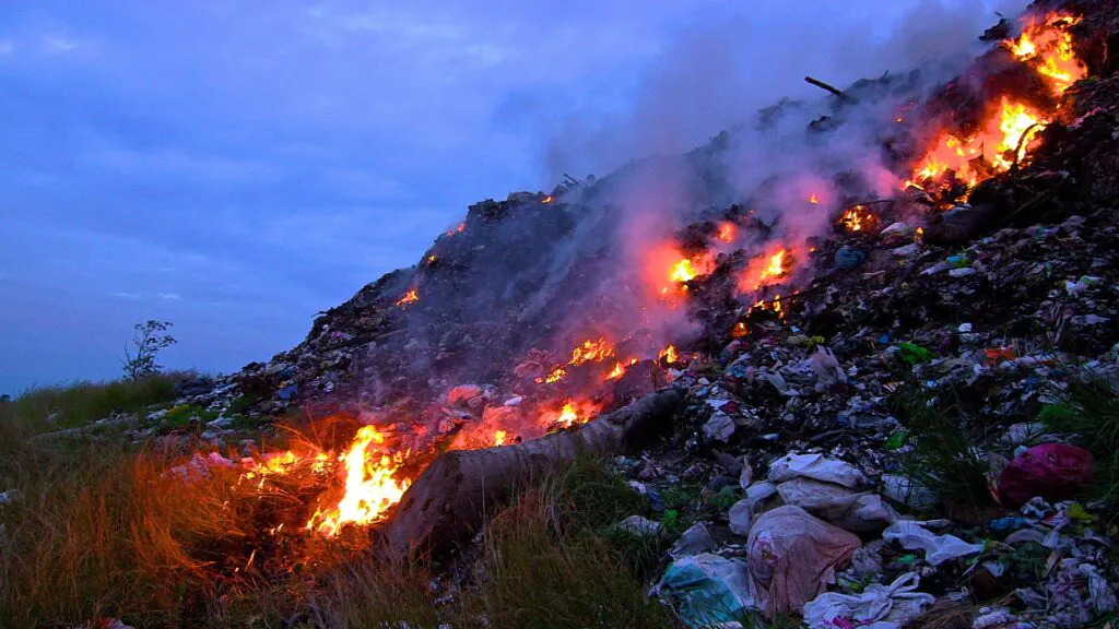 Zdjęcie przedstawiające górę śmieci o zmroku, część śmieci płonie.  