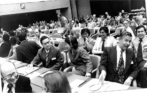 Historia IPCC: konferencja w Villach, 1985. Na zdjęciu widać sale podczas konferencji na temat zmiany klimatu w Villach. Przy długich stołach siedzą osoby, które rozmawiają ze sobą.