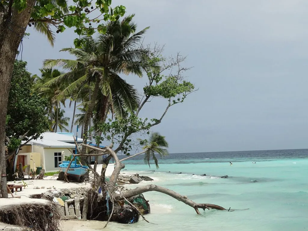 Zdjęcie: skutki zmiany klimatu. Wybrzeże wyspy tropikalnej Maafushi niszczone erozją, widać niewielki domek tuż na brzegu obrywającego się stopniowo gruntu.