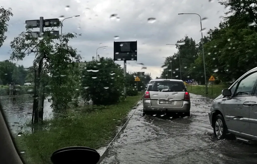 Skutki zmiany klimatu w miastach: powodzie błyskawiczne. Zdjęcie ulicy wykonane z samochodu, na jezdni kilkucentymetrowa warstwa wody.
