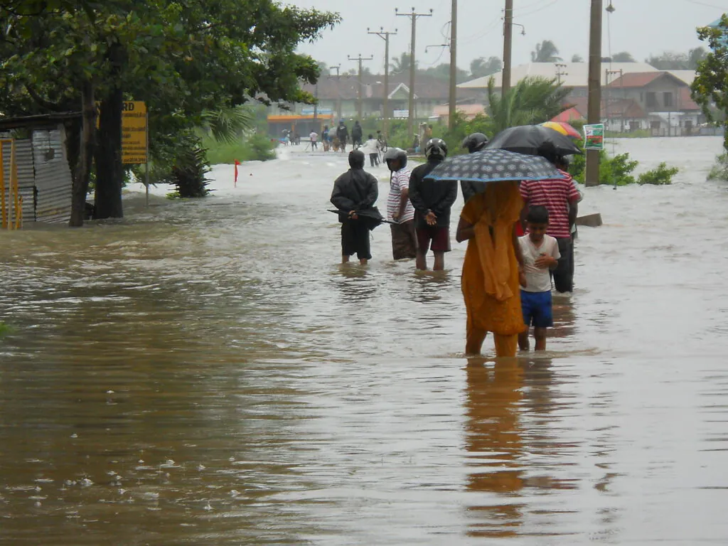 Zdjęcie: powódź na Sri Lance. Widać ludzi brodzących w wodzie po kolana na ulicy niewielkiej miejscowości. 