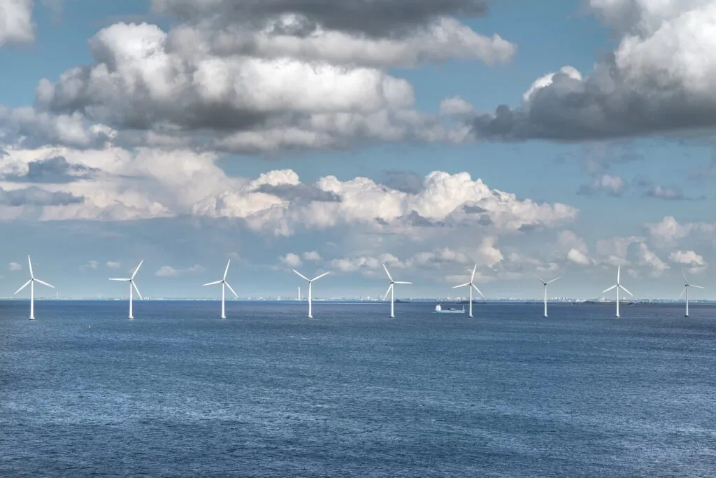 Mitygacja zmiany klimatu. Zdjęcie farmy wiatrowej - widać rząd wiatraków wystających nad powierzchnię morza.