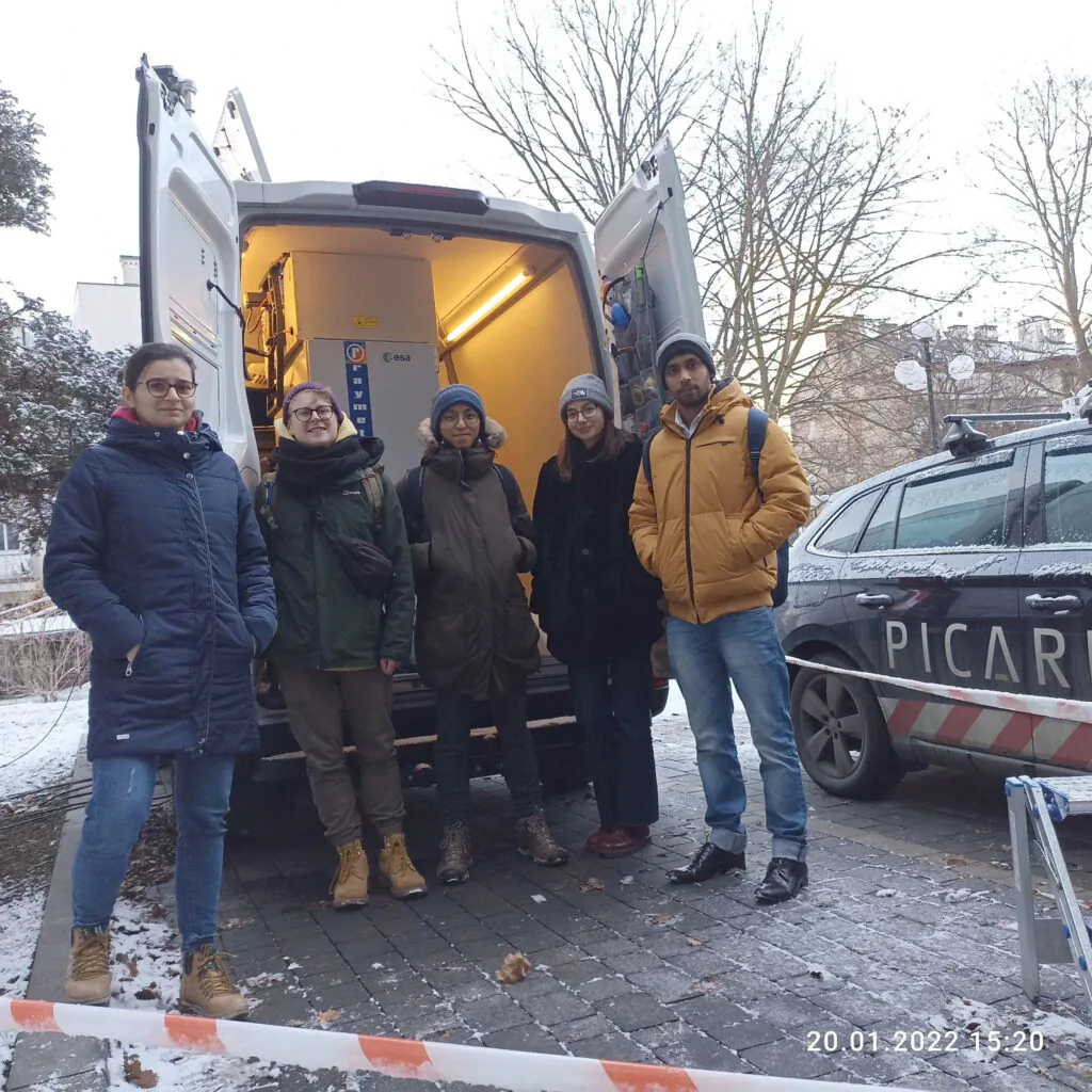 Zdjęcie grupowe: zespół RS-Lab. Pęcioro młodych ludzi przed otwartymi drzwiami furgonetki z lidarem. 