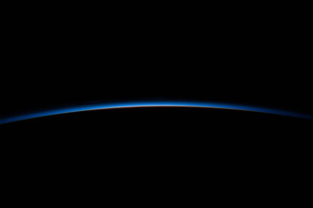 Zdjęcie: widok ze stacji kosmicznej na otulającą Ziemię atmosferę. Na czarnym tle widać niebieski łuk.