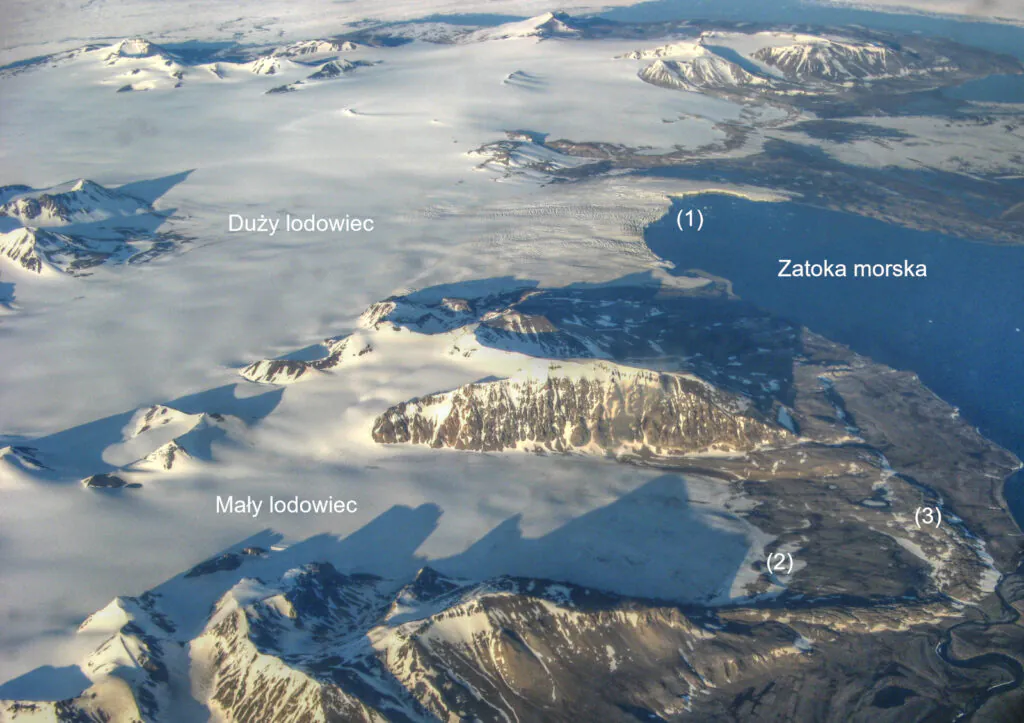 Zdjęcie przedstawia z lotu ptaka fragment Arktyki na którym widać mały lodowiec, który znajduje się w całości na lądzie oraz duży lodowiec, który schodzi do zatoki morskiej.