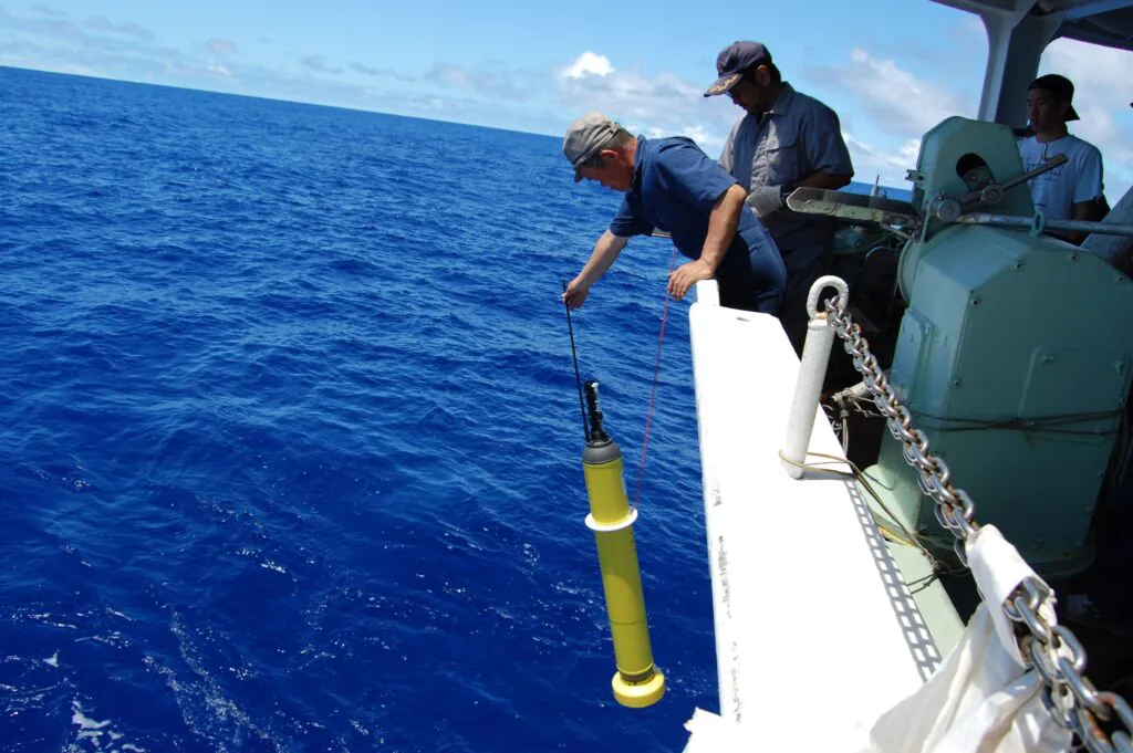 Zdjęcie: naukowiec wychyla się za burtę statku, by umieścić w morzu pływak Argo - żółty cylinder o długości powyżej metra, mieszczący w sobie instrumenty pomiarowe. 