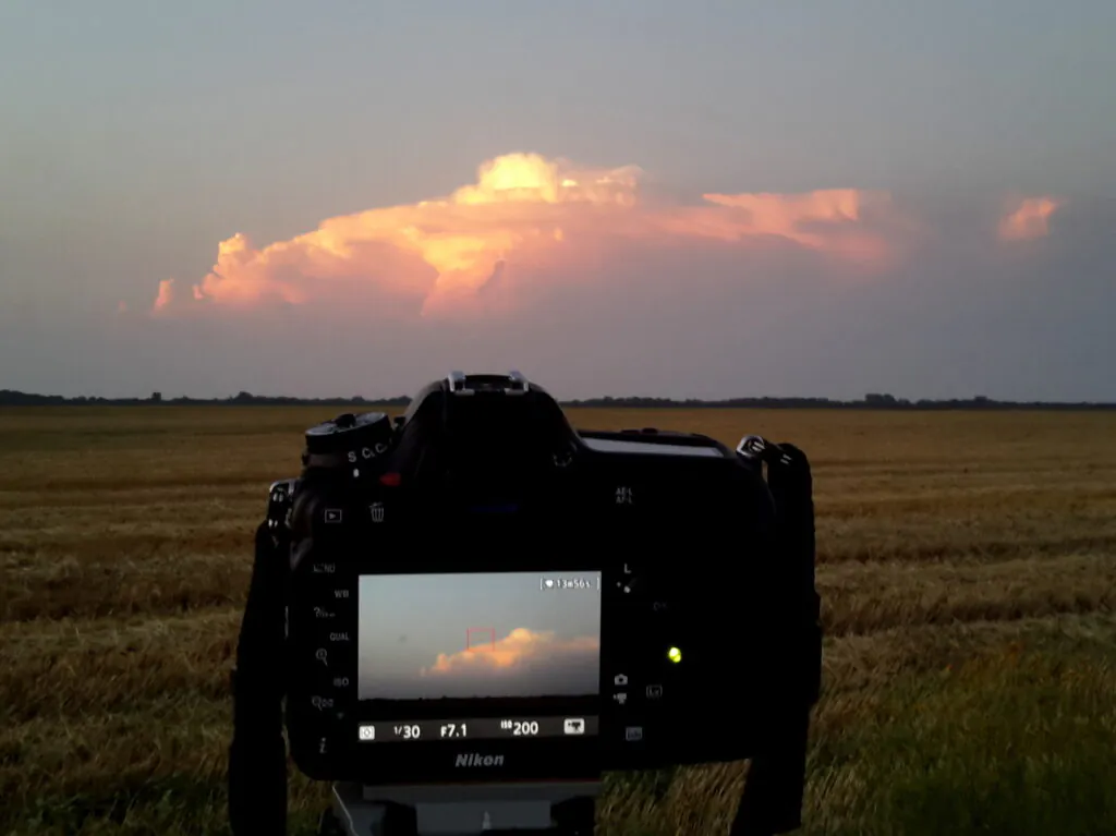 Zdjęcie dekoracyjne: chmura burzowa o zachodzie Słońca. Na pierwszym planie aparat fotograficzny. 