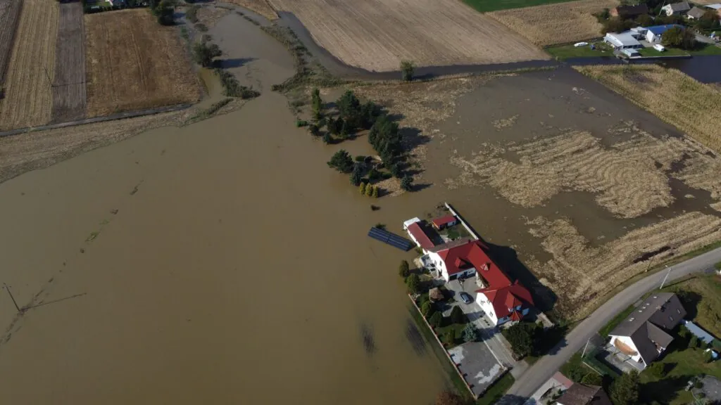 Zdjęcie lotnicze: powódź 2024, Polska. Krajobraz rolniczy, zalane wodą pola, woda podchodząca pod budynek mieszkalny.