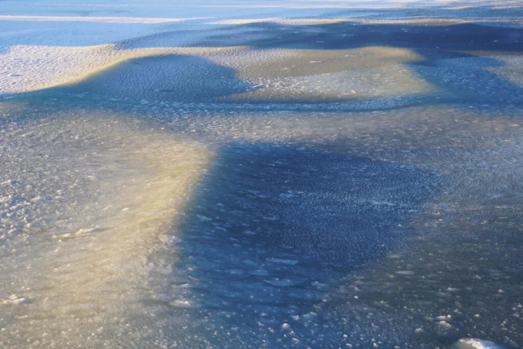 Zdjęcie: fale w śryżu lodowym u wybrzeży Sopotu. Na powierzchni wody dość jednolita mieszanka wody i drobnych kawałków lodu (śryż), z wyraźnymi grzbietami fal.